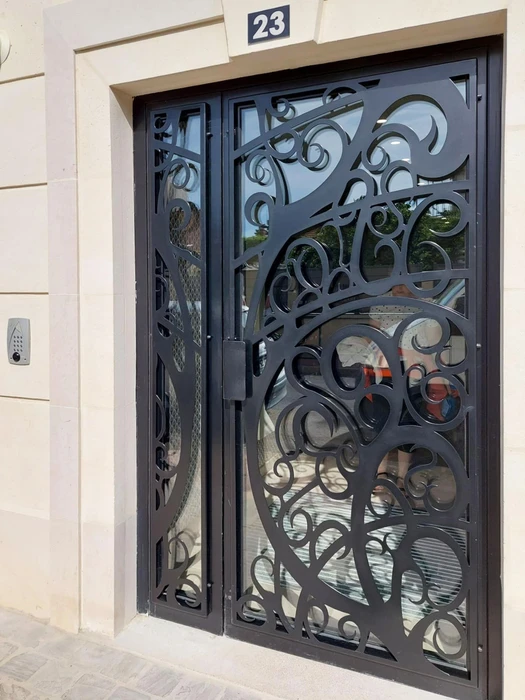Technicien en salopette rouge et t-shirt blanc installe une serrure sur porte d'entrée en bois foncé dans hall d'immeuble moderne