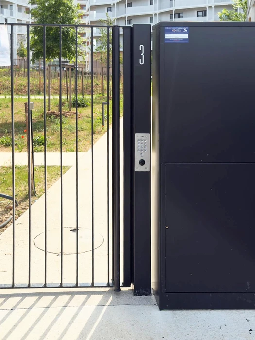Technicien en salopette rouge et t-shirt blanc installe une serrure sur porte d'entrée en bois foncé dans hall d'immeuble moderne