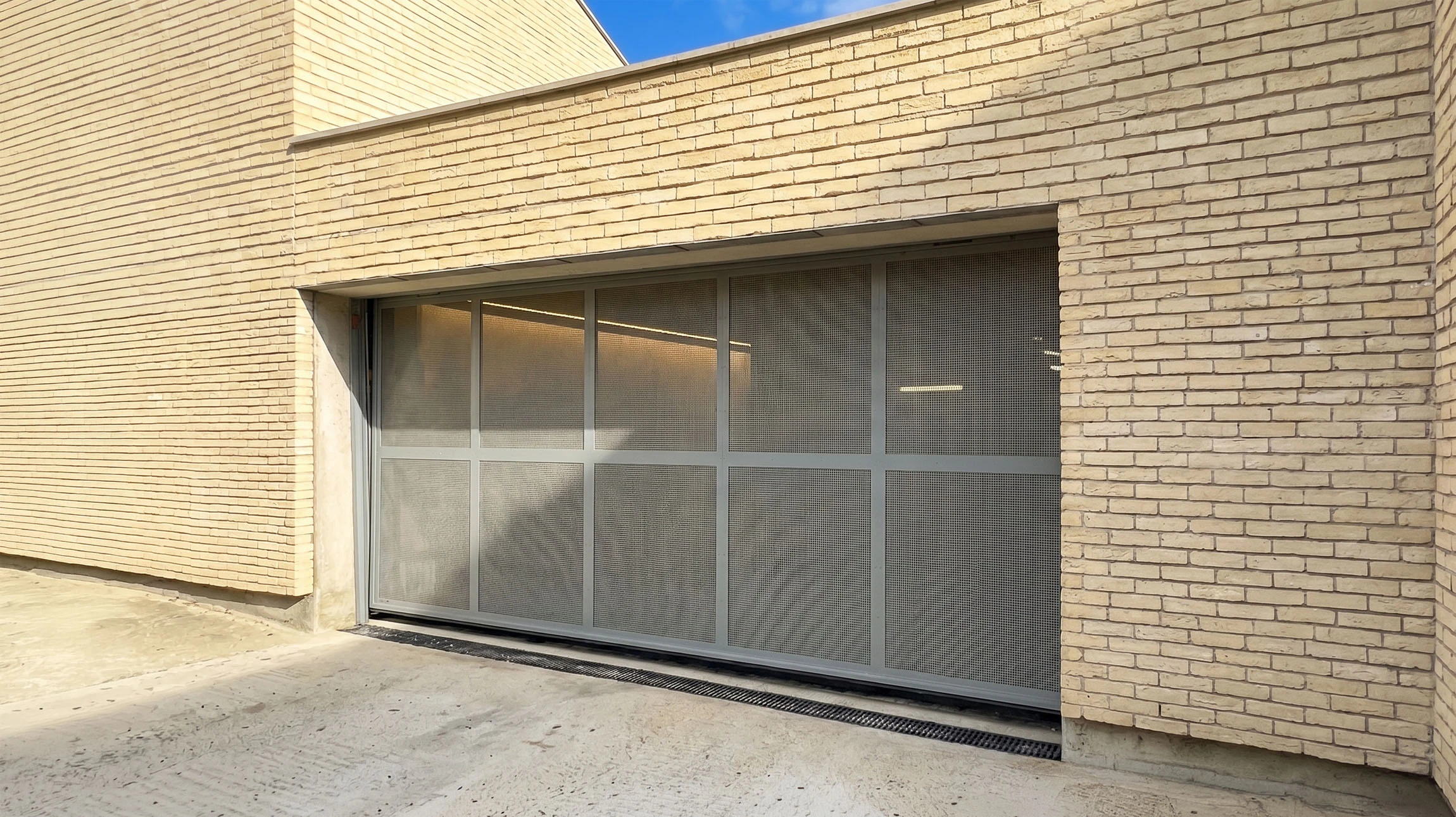 Extérieur commercial avec rideau métallique fermé gris installé dans encadrement béton blanc, sol carrelage beige avec joints apparents